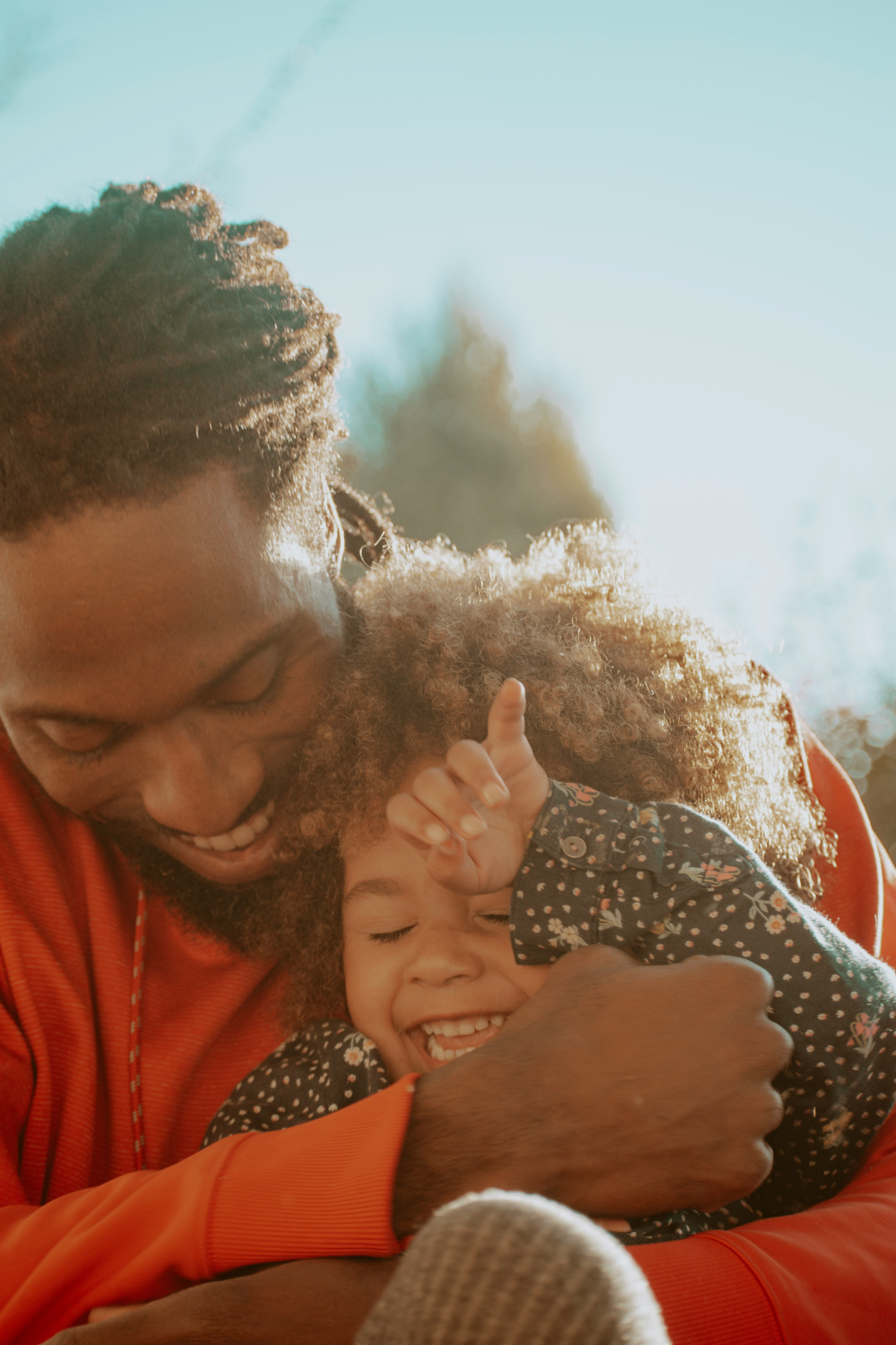 An adult smiling while cuddling a smiling child outdoors